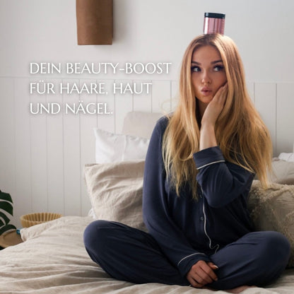 Eine junge Frau mit langen, blonden Haaren sitzt in einem gemütlichen Schlafanzug auf einem Bett. Auf ihrem Kopf balanciert sie eine Dose ‚Beautivin Biotin Boost‘. Links neben ihr steht in weißer Schrift: ‚Dein Beauty-Boost für Haare, Haut und Nägel.‘ Die Szene vermittelt eine entspannte und humorvolle Stimmung.